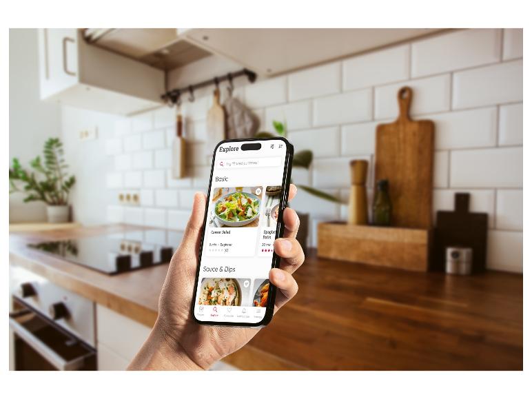 Hand met een telefoon met de Monsieur Cuisine-app open in een lichte keuken Hand met een telefoon met de Monsieur Cuisine-app open in een lichte keuken