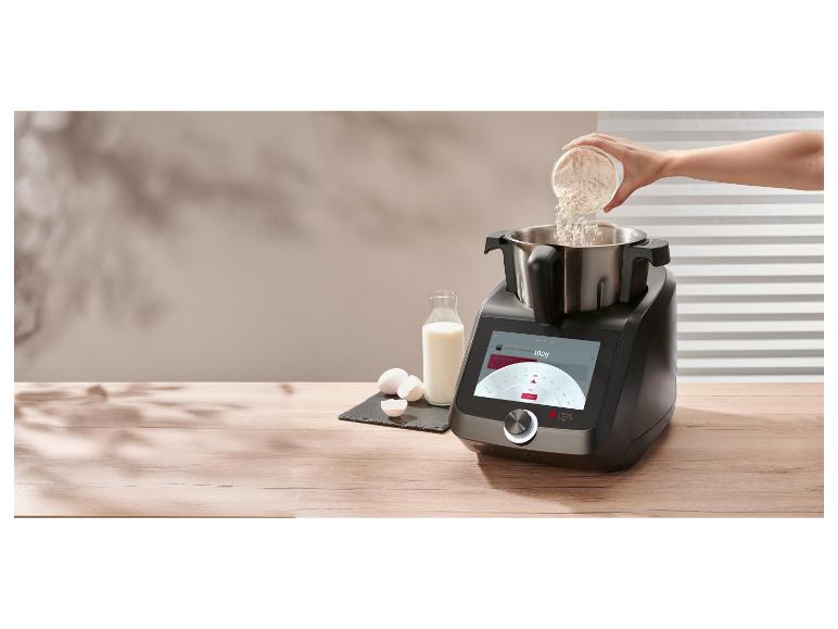 Bloem wordt in de kom van de Lidl keukenmachine geschept, met melk en eieren ernaast op het werkblad Bloem wordt in de kom van de Lidl keukenmachine geschept, met melk en eieren ernaast op het werkblad