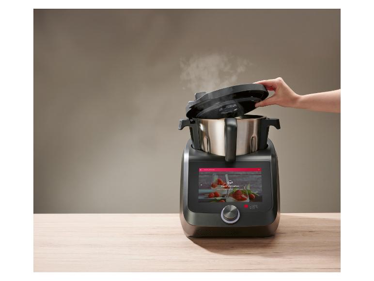 Iemand tilt het deksel van de dampende Monsieur Cuisine smart van Lidl op een houten werkblad Iemand tilt het deksel van de dampende Monsieur Cuisine smart van Lidl op een houten werkblad